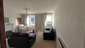A living room with a fireplace, two sofas, a dining table, and a view of the sea through a window. - Kirkcaldy, Fife • Lovely 2 Bedroom Flat • Sea View (Kirkcaldy)