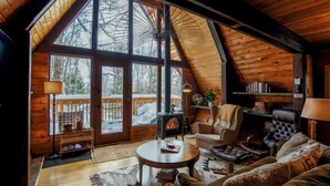 Een gezellig cabin interieur met een groot houten plafond, een open haard, een comfortabele zithoek en uitzicht op een besneeuwd terras.