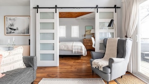 A modern bedroom with a sliding door, a bed, a gray armchair, and a view of the outside. - Lakefront Getaway | Hot Tub, Fire Pit & Sunsets (Selkirk)