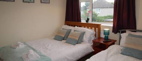 A hotel room with two single beds, a nightstand with a lamp, and a window with curtains.