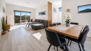 Una sala de estar moderna con un sofá, una mesa de comedor con sillas y vistas a un patio exterior a través de un ventanal.