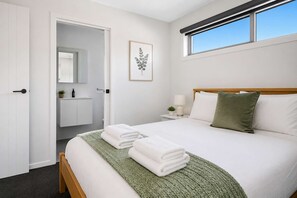 Quarto moderno com cama, mesa de cabeceira, abajur, manta verde e quadro na parede.