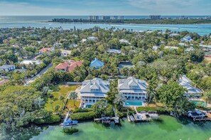 An aerial view of a coastal residential area with houses, a marina, and a clear view of the ocean.