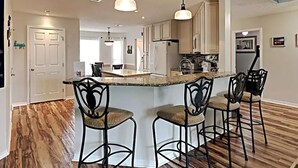 Una cocina moderna con una isla central, taburetes de bar, iluminación colgante y suelo de madera.
