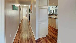 Un pasillo con piso de madera que conduce a una cocina con armarios blancos.