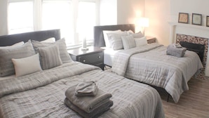 A hotel room with two beds, a nightstand, a lamp, and a fireplace. - Mathilda Street Trio - City View - 2 Queen Beds (Pittsburgh)