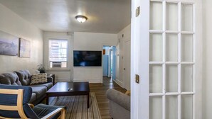 Una sala de estar con sofá, una mesa de centro, televisor y una puerta con paneles de vidrio esmerilado.