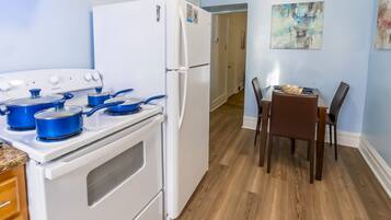 A kitchen with a white refrigerator, a stove with blue pots, a dining table with chairs, and a painting on the wall.