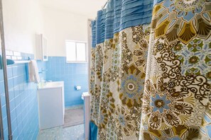 A bathroom with blue tiled walls, a white sink, and a patterned shower curtain. - Mathilda Street Trio - Stylish 2BR Apt (Pittsburgh)