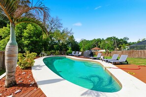 A swimming pool with a wooden deck, lounge chairs, and a palm tree.