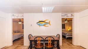 En matplats med ett träbord och stolar, ett konstverk med fiskmotiv på väggen och en takfläkt.
