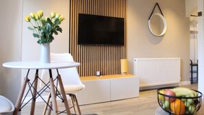 A modern living room with a round table, a sofa, a TV mounted on a wooden panel wall, a round mirror, and a fruit bowl. - Modern Stylish Apartment with central access (Perth)