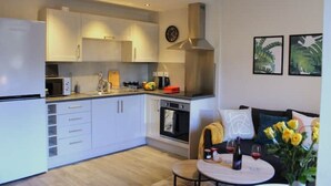 A modern kitchen with white cabinets, a built-in oven, and a stove. There is a dining area with a table and chairs, and a sofa with a vase of flowers. - Modern Stylish Apartment with central access (Perth)