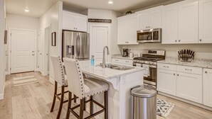 A modern kitchen with white cabinets, stainless steel appliances, and a central island with bar stools. - Sand, Sun & Fun! (Washington)