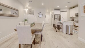 A modern kitchen with white cabinets, a stainless steel refrigerator, and a wooden dining table with upholstered chairs. - Sand, Sun & Fun! (Washington)