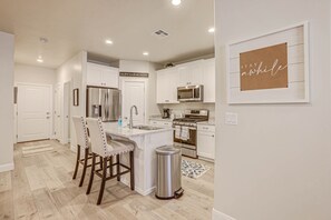 A modern kitchen with white cabinetry, stainless steel appliances, and a central island with bar stools.