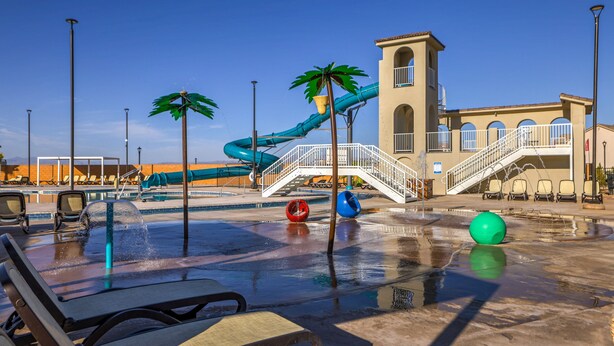 A water park with a blue water slide, palm trees, and a pool area with lounge chairs. - Sand, Sun & Fun! (Washington)