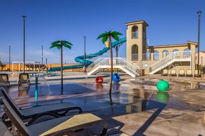 A water park with a blue water slide, palm trees, and a pool area with lounge chairs.