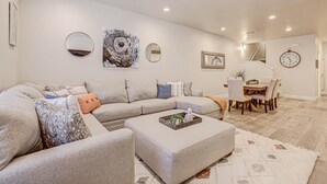 A modern living room with a sectional sofa, ottoman, and dining area with a wooden table and chairs. - Sand, Sun & Fun! (Washington)