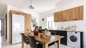Een moderne keuken met houten kastjes, een ingebouwde wasmachine en een eethoek met een tafel en stoelen.