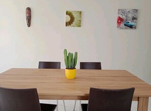 Una mesa de comedor con una maceta amarilla de cactus, dos sillas y tres adornos de pared.