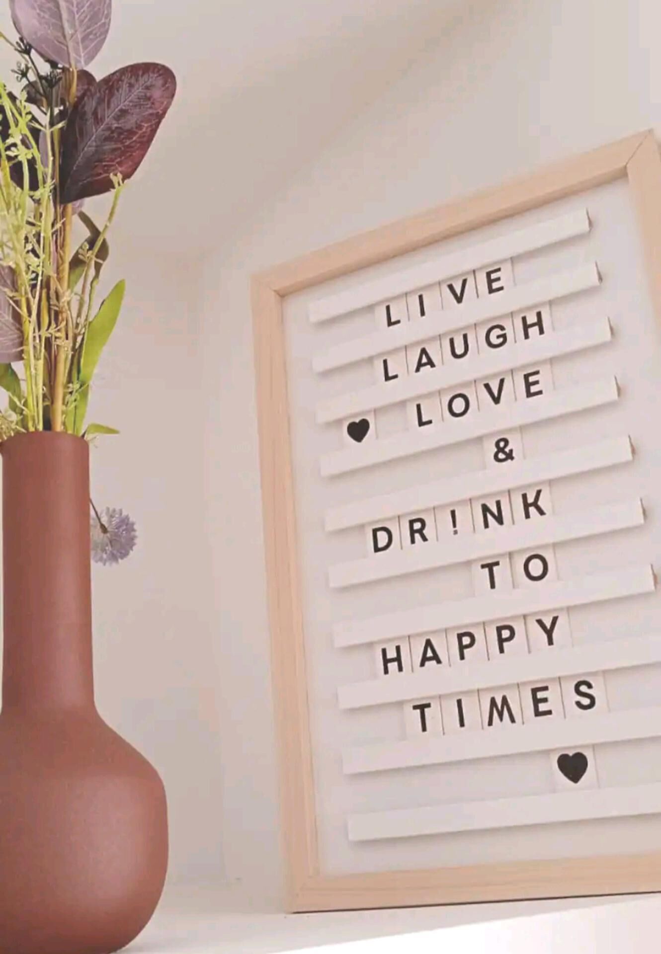 A framed inspirational message with a vase of flowers to the left.
