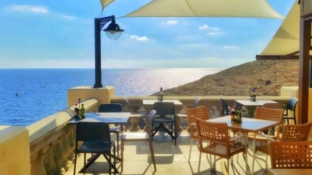 Een terras met tafels en stoelen, met uitzicht op zee.