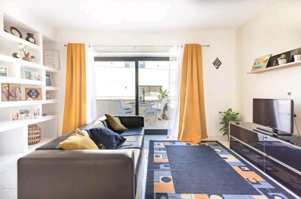 Una sala de estar con un sofá, televisor y estanterías con diversos objetos.