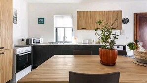 Een moderne keuken met houten kastjes, een inbouwoven, een spoelbak en een eettafel met stoelen.