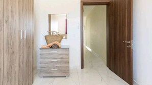 Een gang met een houten garderobe, een spiegel, een rieten mand en een deur naar een andere kamer.