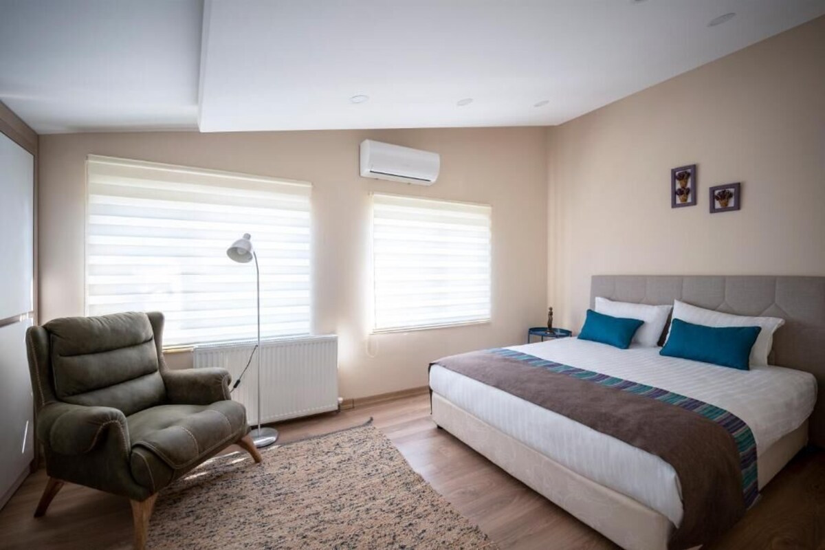 Un dormitorio con cama, una silla, un radiador y dos ventanas con persianas.