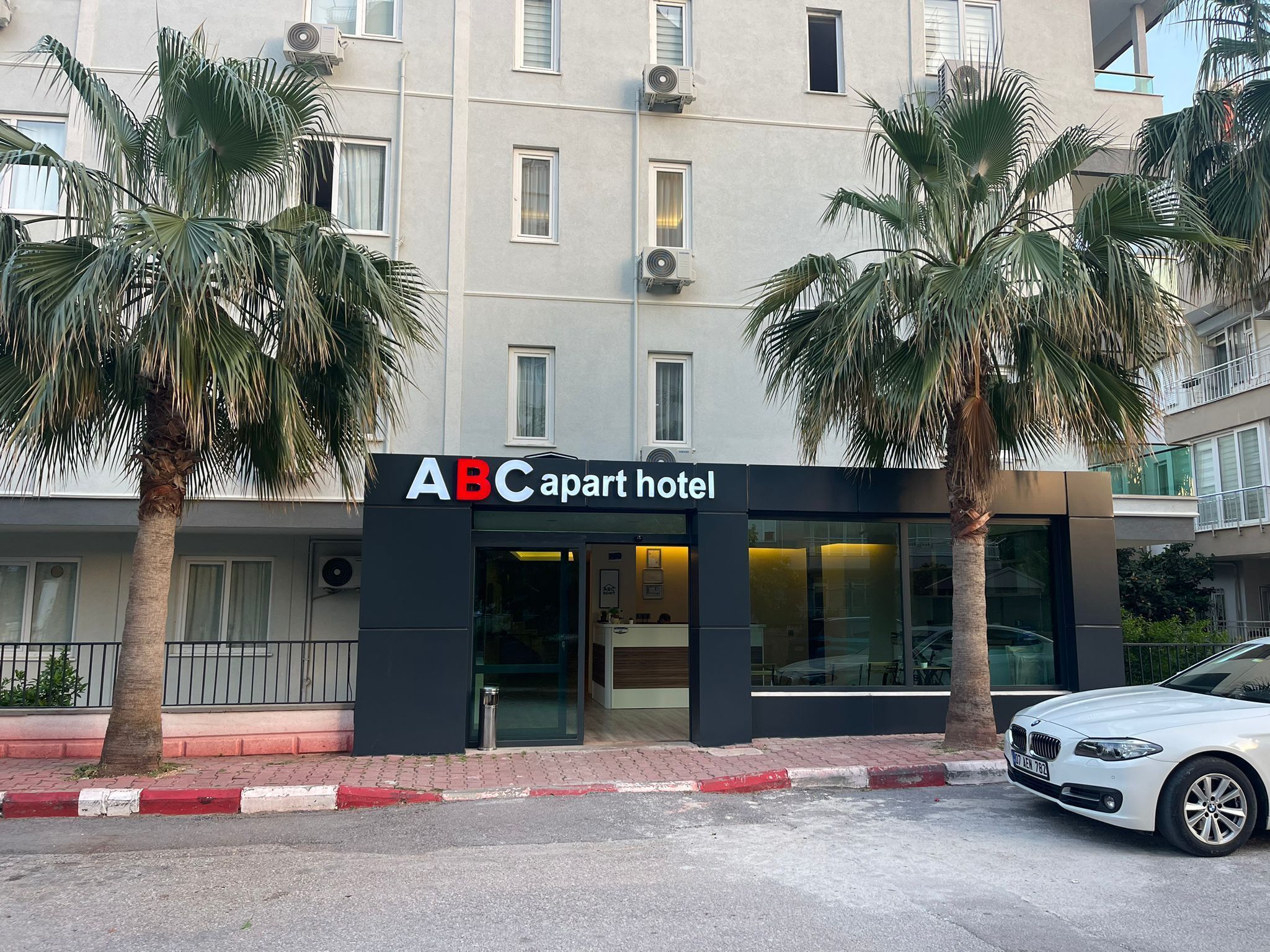 Ein Gebäude mit einem Schild, auf dem 'ABC apart hotel' steht, und Palmen davor.