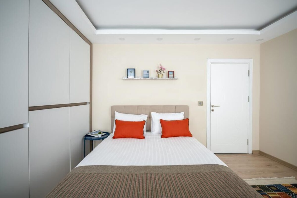 Un dormitorio con cama, mesita de noche, una puerta y estante con fotografías.