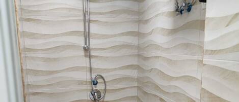 A shower with a wavy tile wall and a tiled floor.