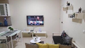 Ein modernes Wohnzimmer mit flachbildfernseher an der Wand, einer Couch mit Kissen, einem kleinen Couchtisch und einem Essbereich mit Stühlen und Tisch.