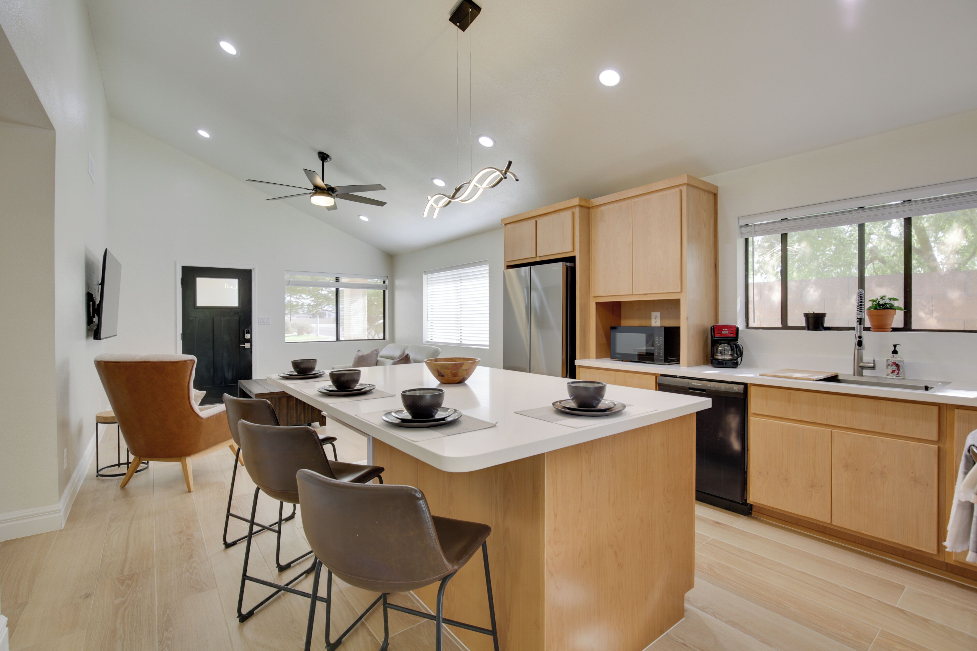 Una cocina moderna con una isla central, taburetes de bar, armarios de madera, un refrigerador y un lavavajillas.