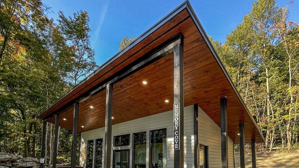 Un edificio moderno con techo de madera, amplias ventanas y un patio cubierto con mobiliario exterior.