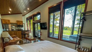 Un dormitorio amplio con una cama grande, techo de madera y vistas a un paisaje verde a través de amplias ventanas.