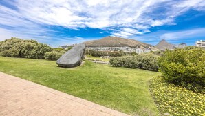A landscaped area with a large stone sculpture, a grassy field, and a hill with a pyramid-like structure in the background. - Stylish and Modern Studio in the Beachfront (Cape Town)