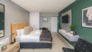 A modern bedroom with a large bed, bedside tables, a desk, a chair, a TV, and a green accent wall. - Stylish and Modern Studio in the Beachfront (Cape Town)