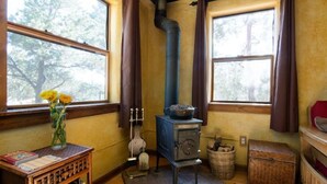 Ein gemütlicher Raum mit Kamin, einem Vorhangfenster, einer Blumenvase und einem kleinen Tisch mit Büchern.