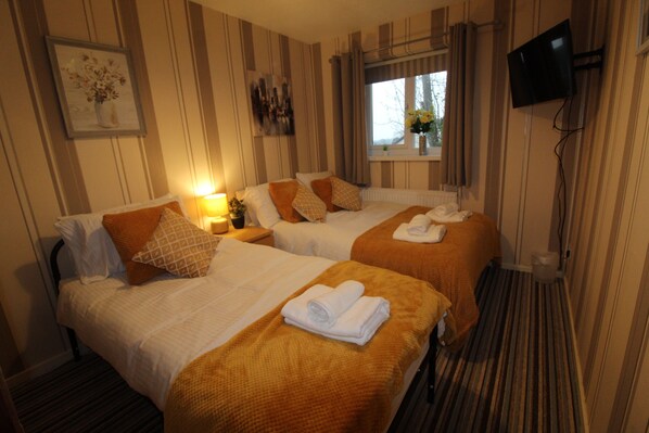 A hotel room with two beds, striped wallpaper, a TV mounted on the wall, and a window with curtains. - Aspley House (Sutton-in-Ashfield)