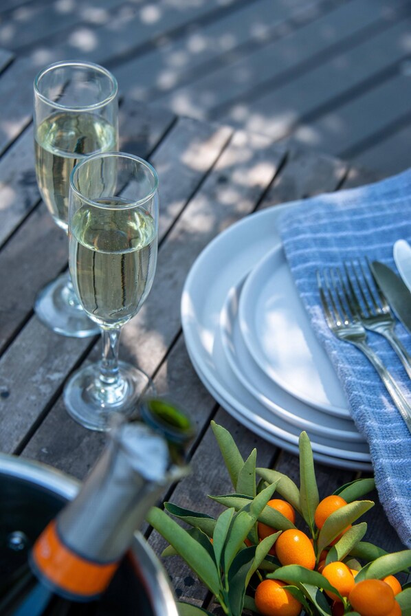 Una mesa dispuesta con dos copas de vino blanco, una botella, un plato con tenedor y cuchillo, y una servilleta.