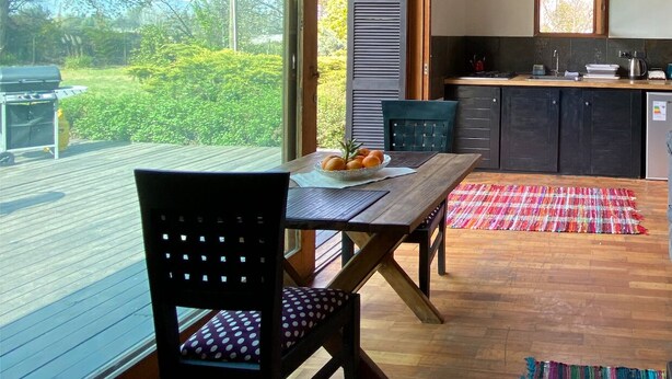A modern kitchen with a large window, wooden flooring, and a dining area with a table and chairs. - Chena Magica (Calera de Tango)