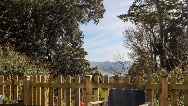 A wooden deck with a view of mountains, a bottle of wine, and three glasses on a table. - Plas Elyn (Beaumaris)