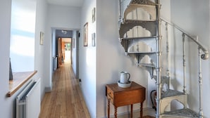 A wooden floor hallway with a staircase featuring ornate metal railings and a small wooden table with a pitcher and bowl. - Plas Elyn (Beaumaris)