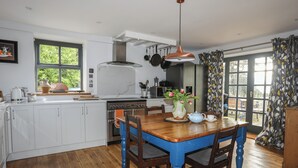 A kitchen with white cabinets, a wooden dining table, and a blue chair. - Plas Elyn (Beaumaris)