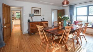 A dining area with a wooden table and chairs, a pendant light, and a view of the outdoors through a window. - Plas Elyn (Beaumaris)
