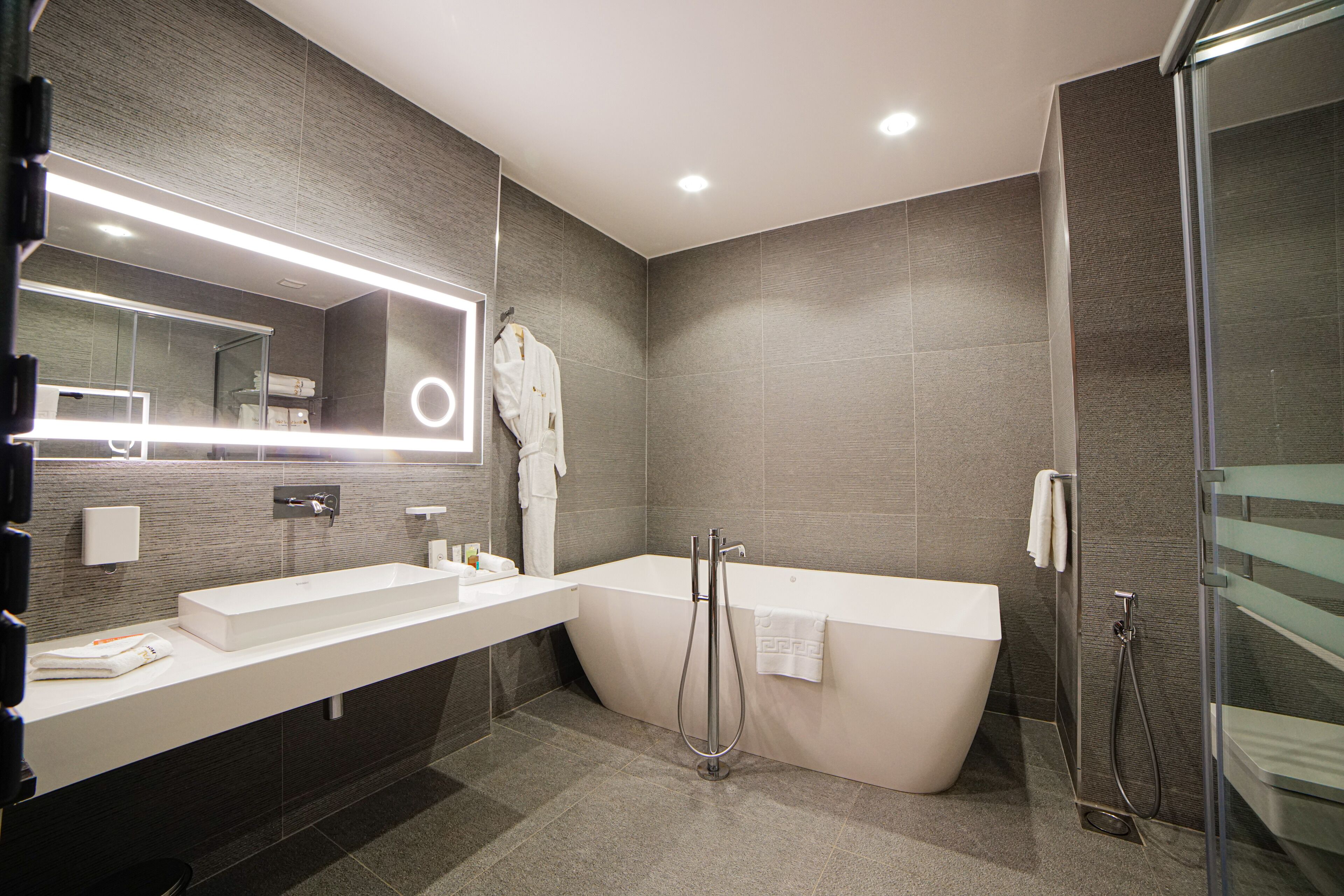 Un baño moderno con un espejo grande, lavamanos dobles, una bañera independiente y una cabina de ducha de vidrio.