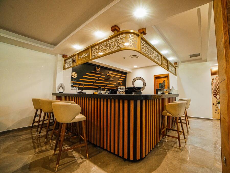 Un'area bar con un bancone in legno e sgabelli, un soffitto decorativo e una reception con sfondo nero.